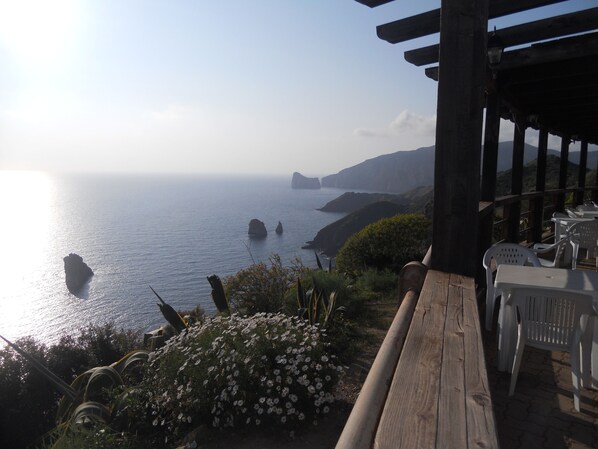 A coastal view with a wooden deck and white plastic chairs, overlooking the sea and distant cliffs. - Villa Red Coral: sleeps 4, shared swimming pool, parking, (Iglesias)