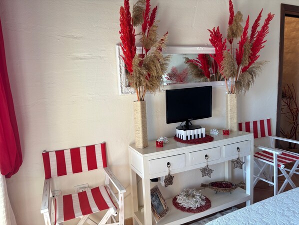 A room with a white TV stand, a red and white striped chair, and decorative plants.