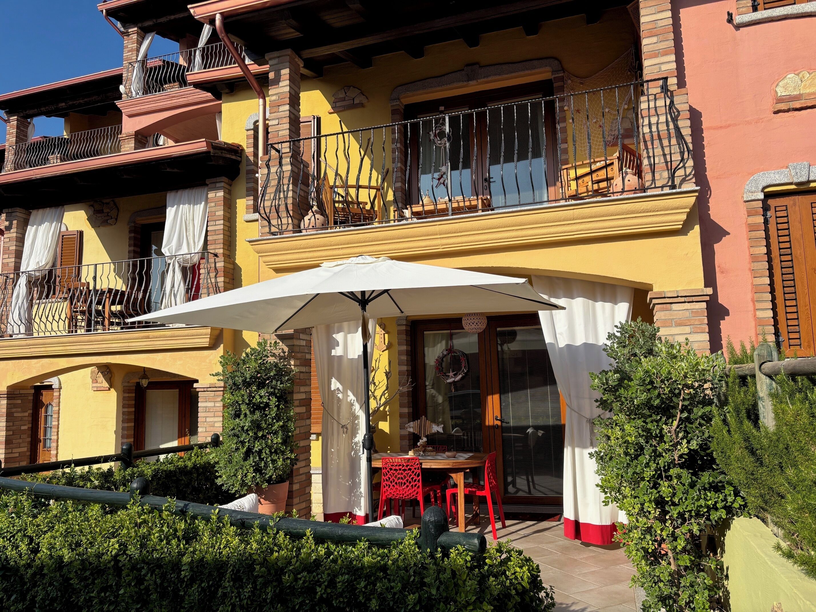 A two-story building with a balcony, a table with chairs, and a large umbrella.