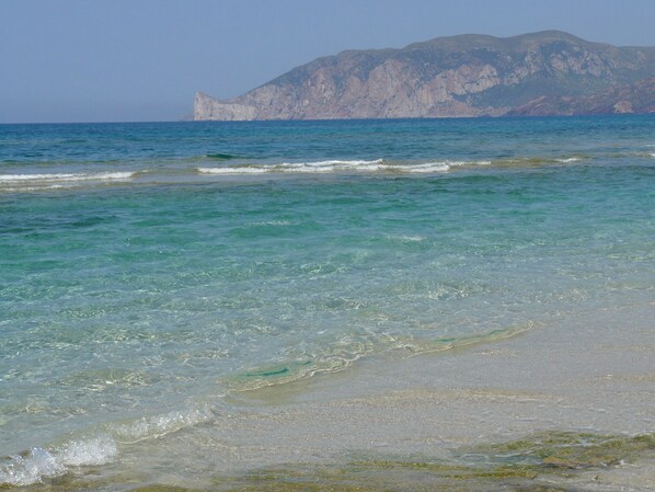 Een strand met helder turquoise water en een rotsachtige berg op de achtergrond.