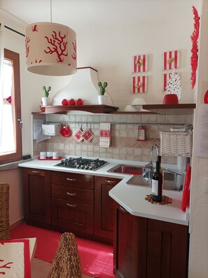 A modern kitchen with wooden cabinets, a gas stove, a sink, and a hanging light fixture.