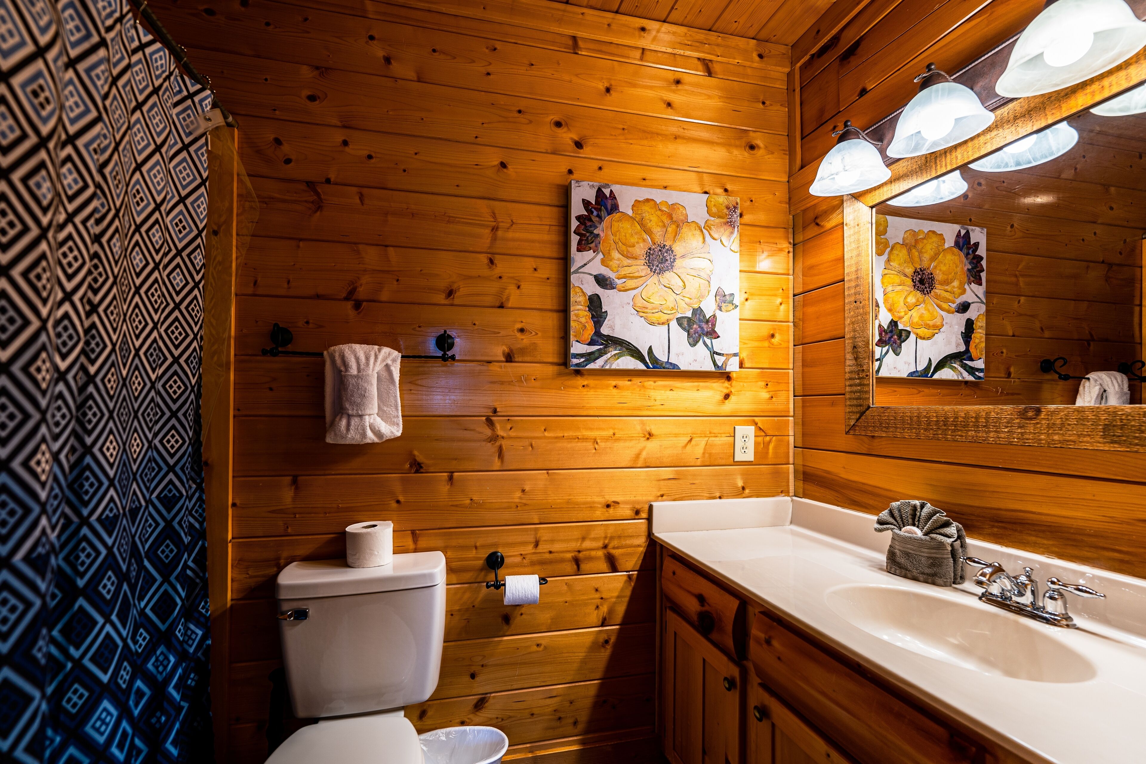 Un baño de cabaña de madera con inodoro, lavabo y espejo con iluminación.