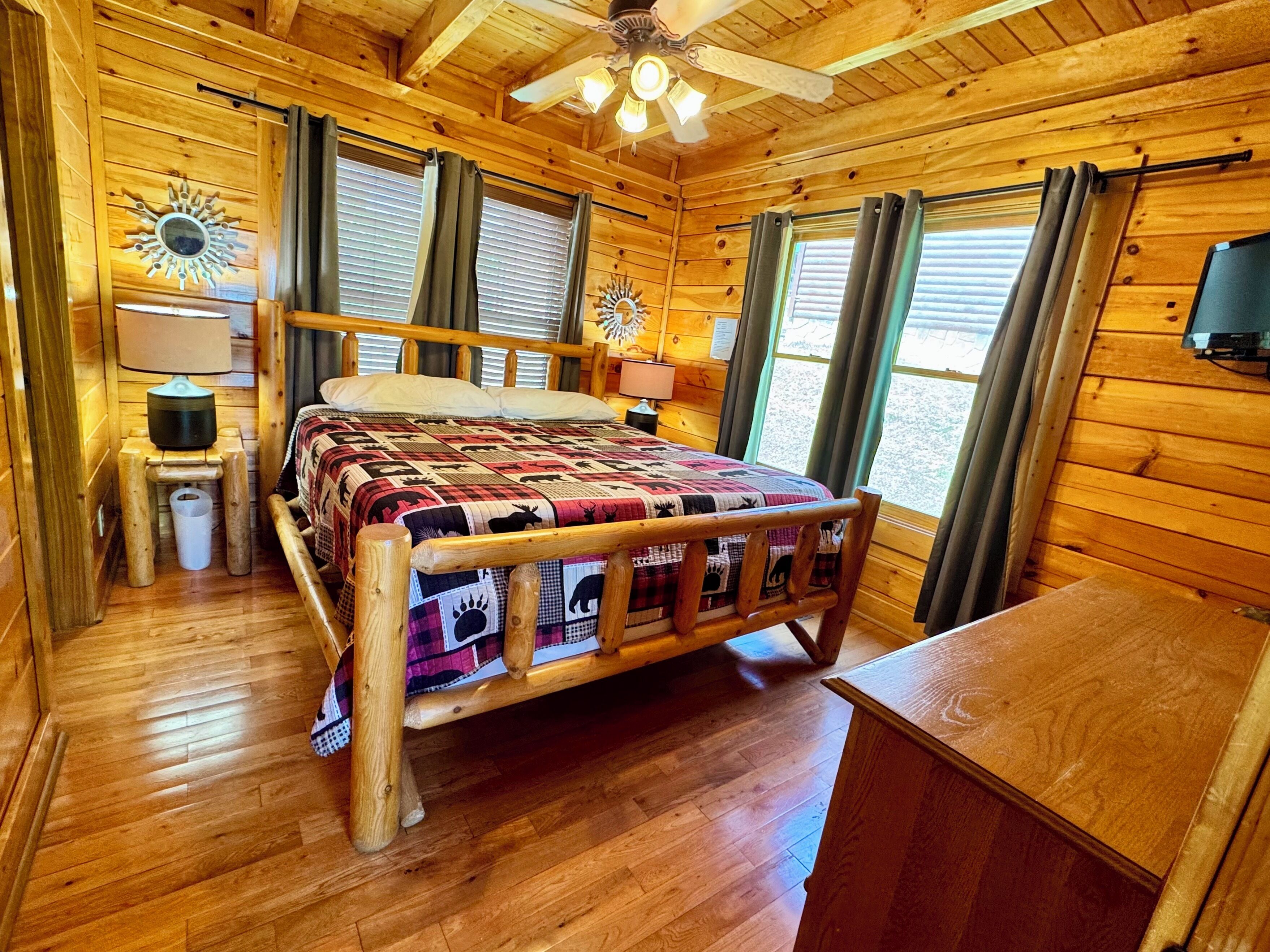 A wooden cabin bedroom with a bed, a nightstand, a lamp, and a ceiling fan.