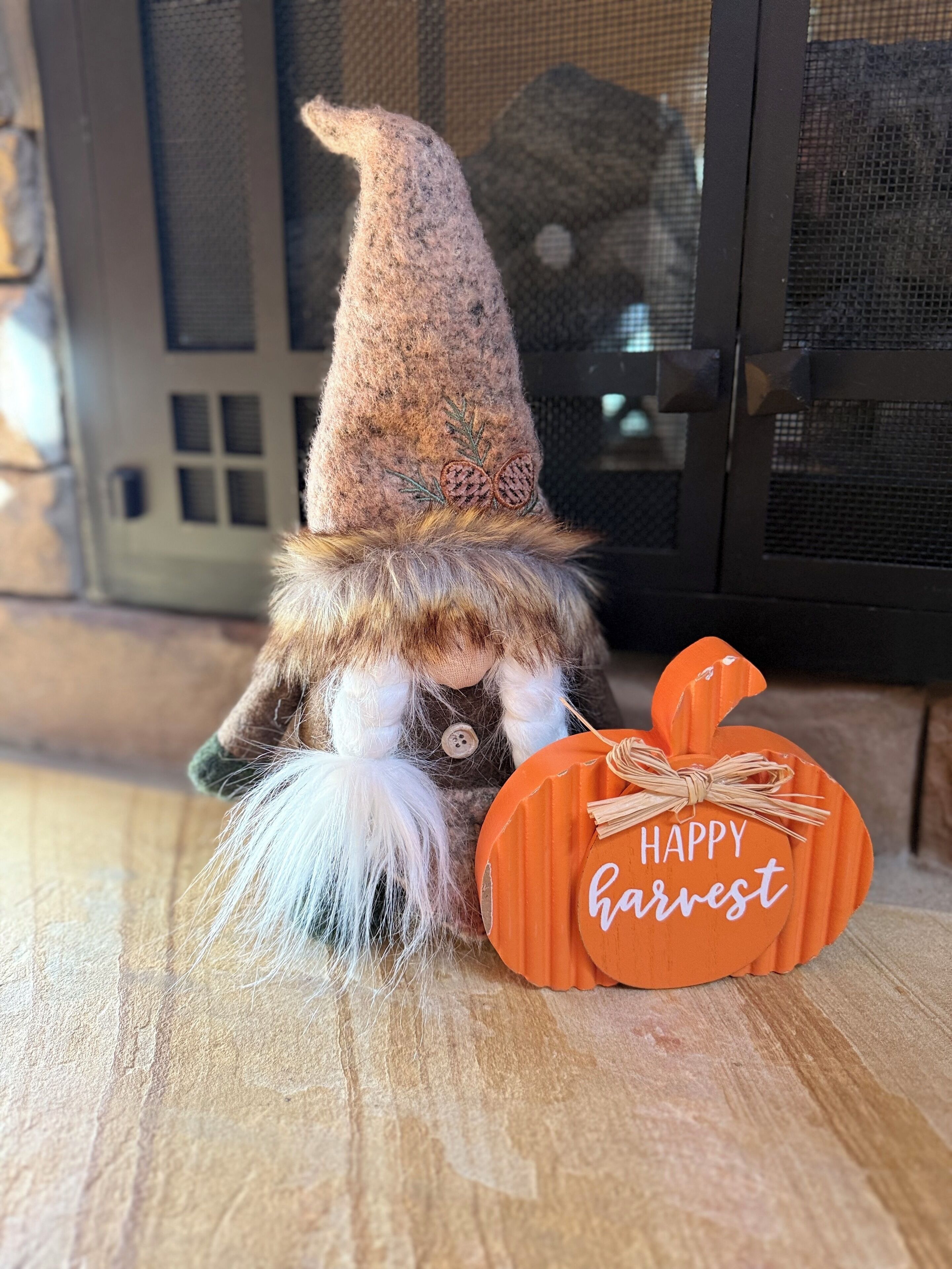 Una figurita de gnomo al lado de un adorno con forma de calabaza que dice 'Happy Harvest'.