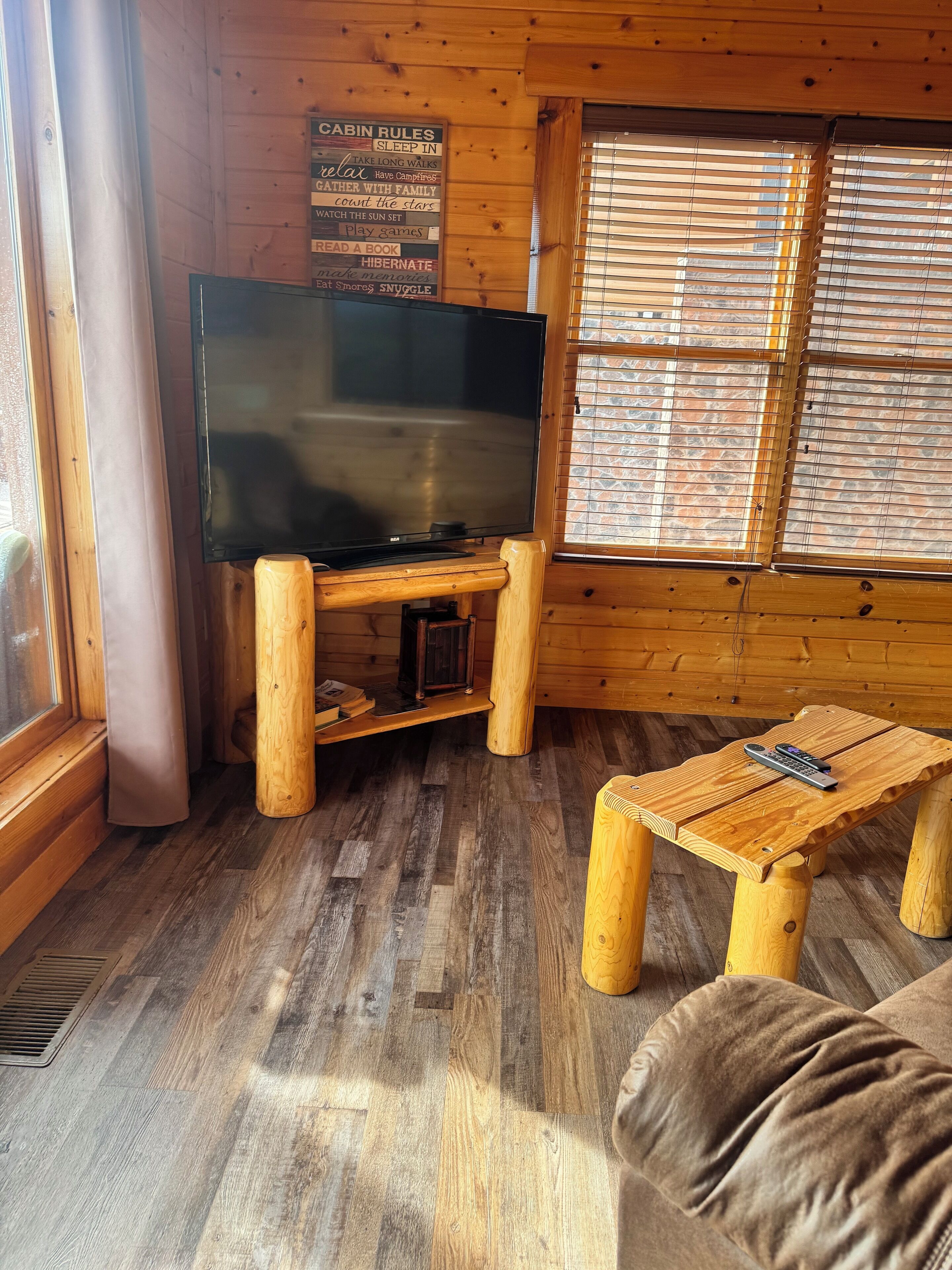 A cabin interior with a wooden TV stand, a couch, and a window with blinds.