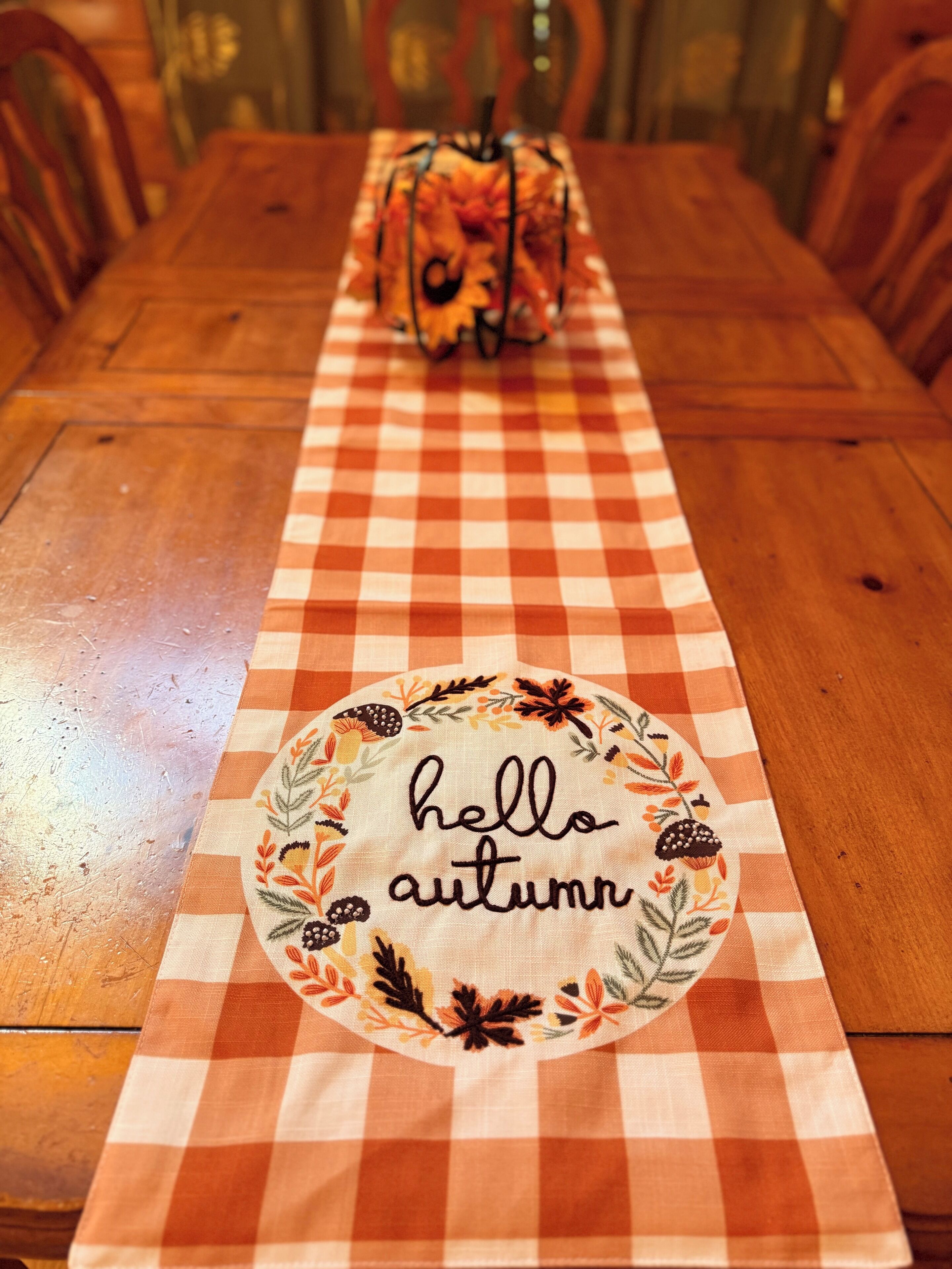 Una mesa de comedor con mantel a cuadros y un posavasos decorativo que dice 'hello autumn'.