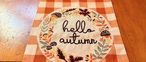 Una mesa de comedor con mantel a cuadros y un posavasos decorativo que dice 'hello autumn'.