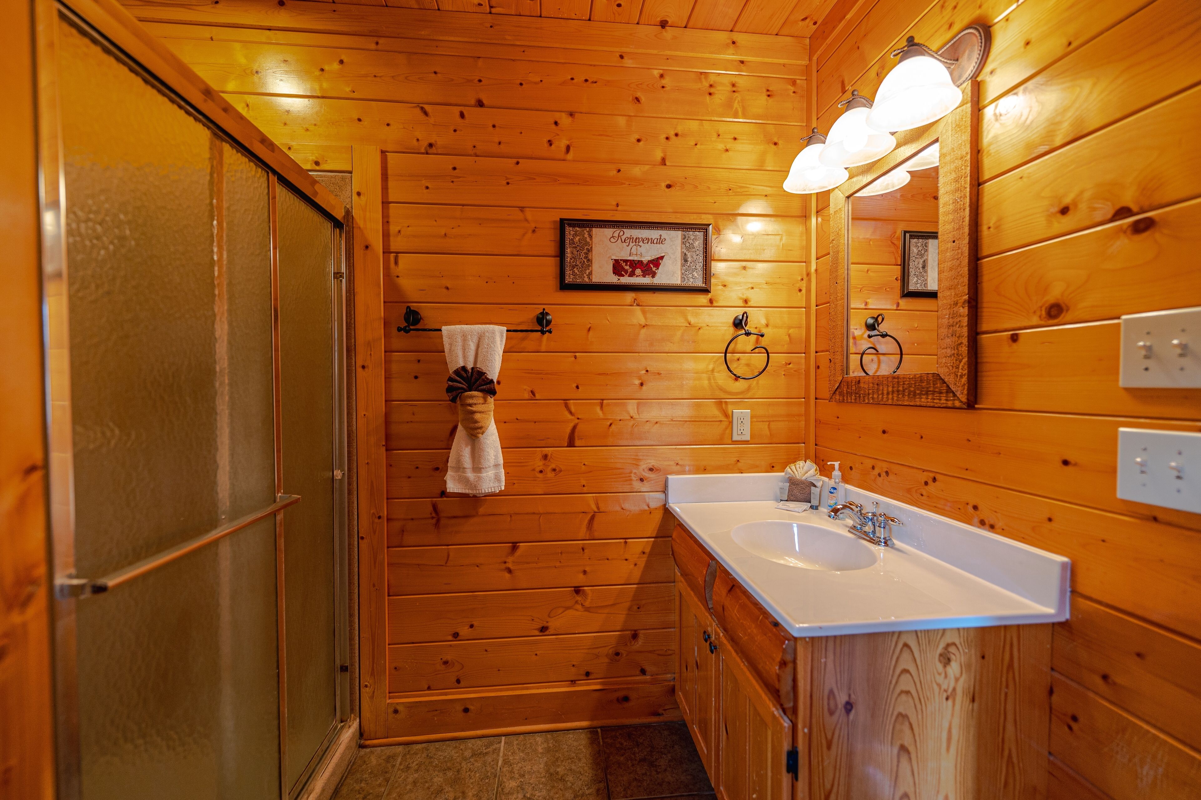 A wooden-paneled bathroom with a glass shower door, a sink, and a mirror.