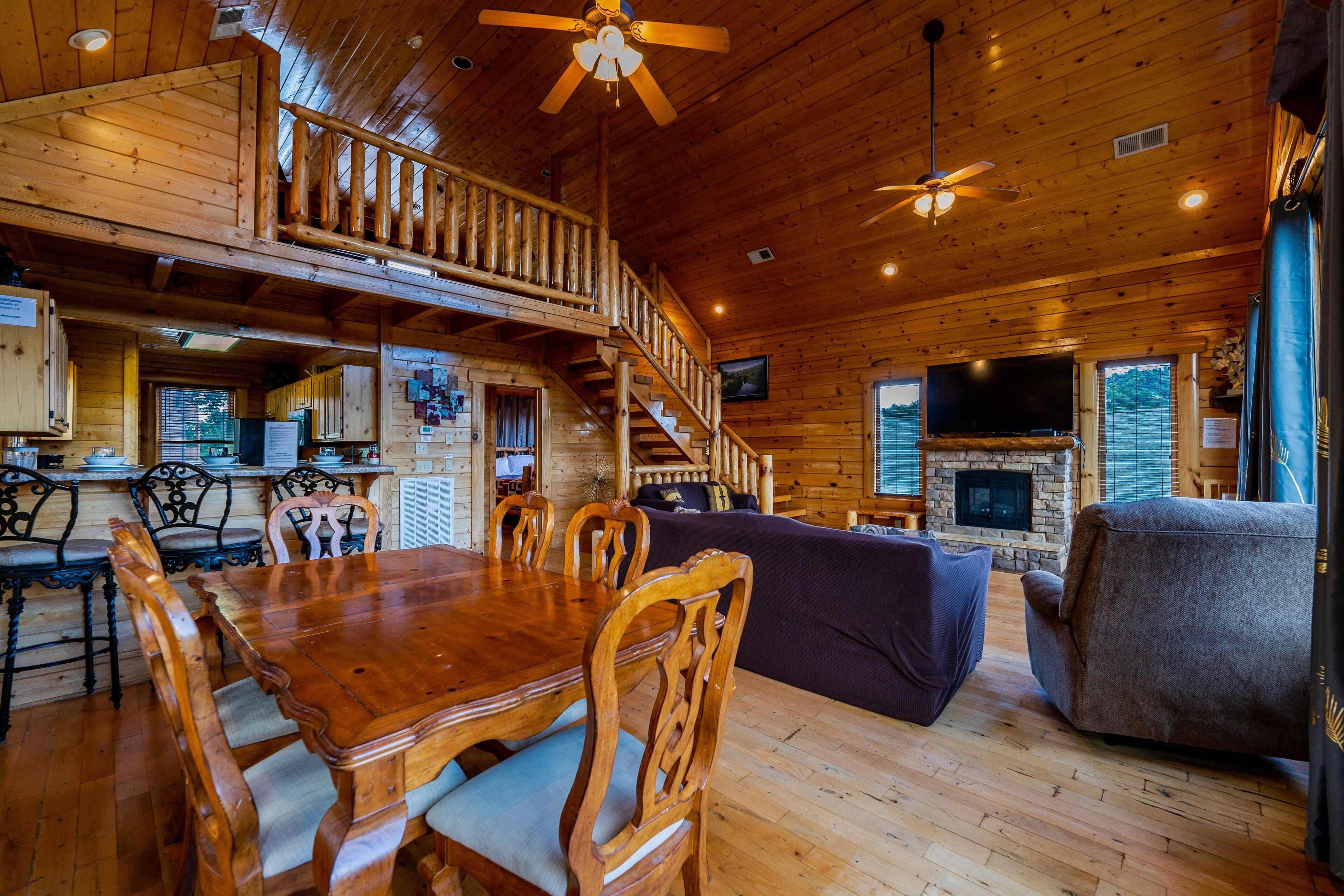 A wooden cabin interior with a dining area, staircase, living room, and fireplace.