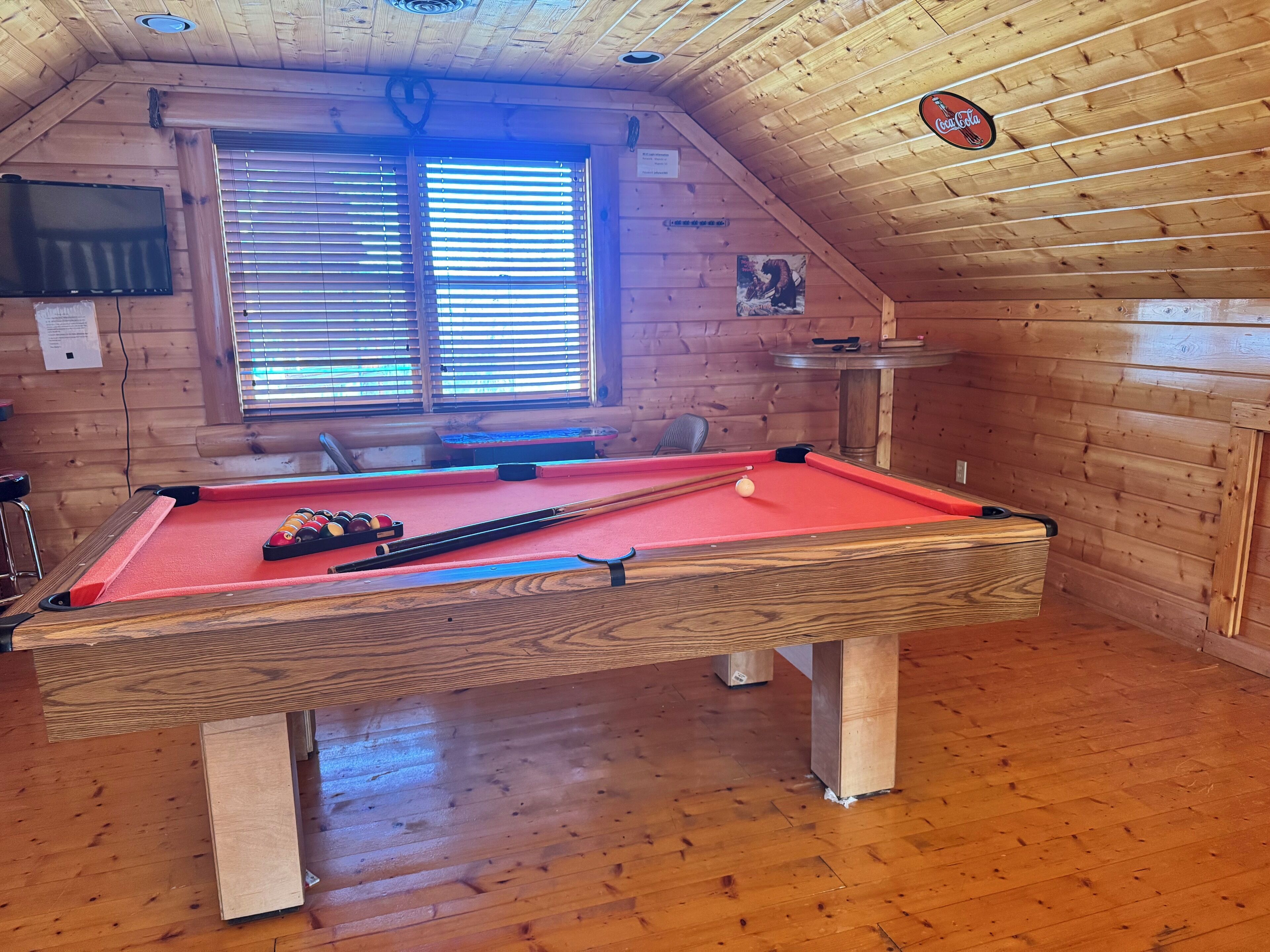 Een pooltafel in een houten kamer met een raam en een Coca-Cola bord.
