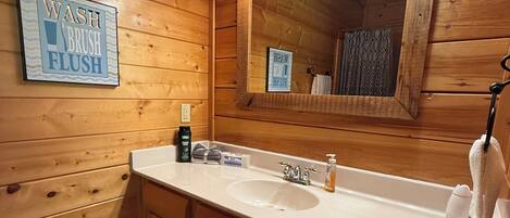 Bany d'una cabana de fusta amb un lavabo, un mirall i un cartell que diu 'WASH BRUSH FLUSH'.