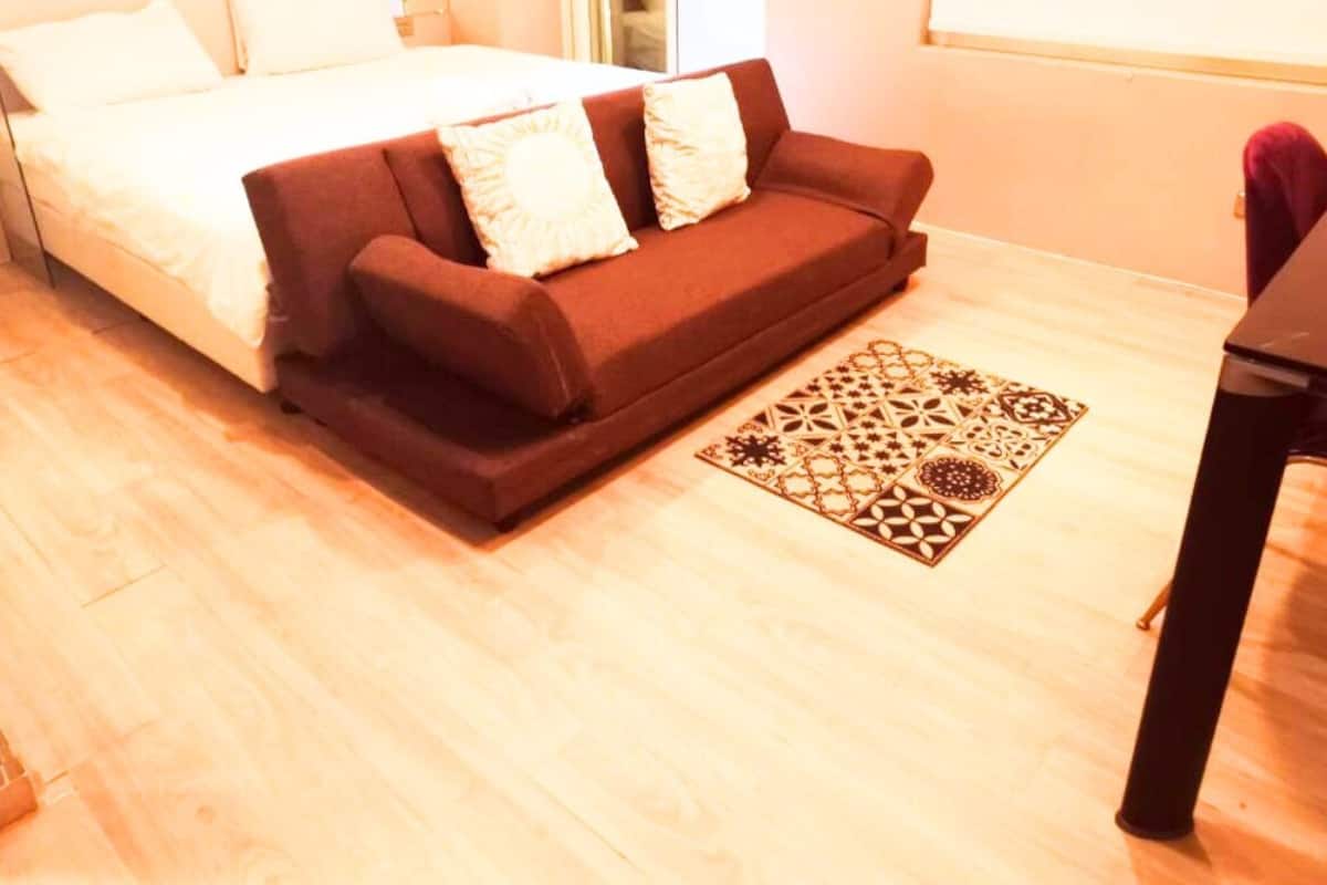 A bedroom with a bed, a brown sofa, a patterned rug, and a desk.