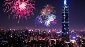 Un paisaje urbano con una torre destacada iluminada por la noche, rodeada de fuegos artificiales.