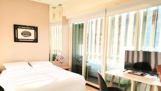 Habitación de hotel con cama, escritorio y silla, televisor y un amplio ventanal con cortinas.