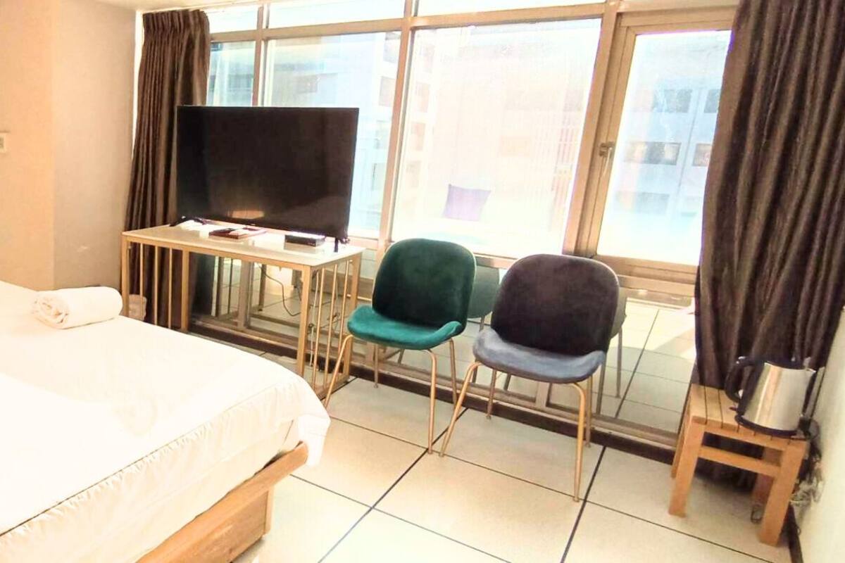 A hotel room with a bed, a desk with a TV, two chairs, and a window with curtains.
