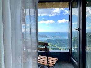 A balcony with a wooden bench, a glass door, and a view of a coastal landscape.