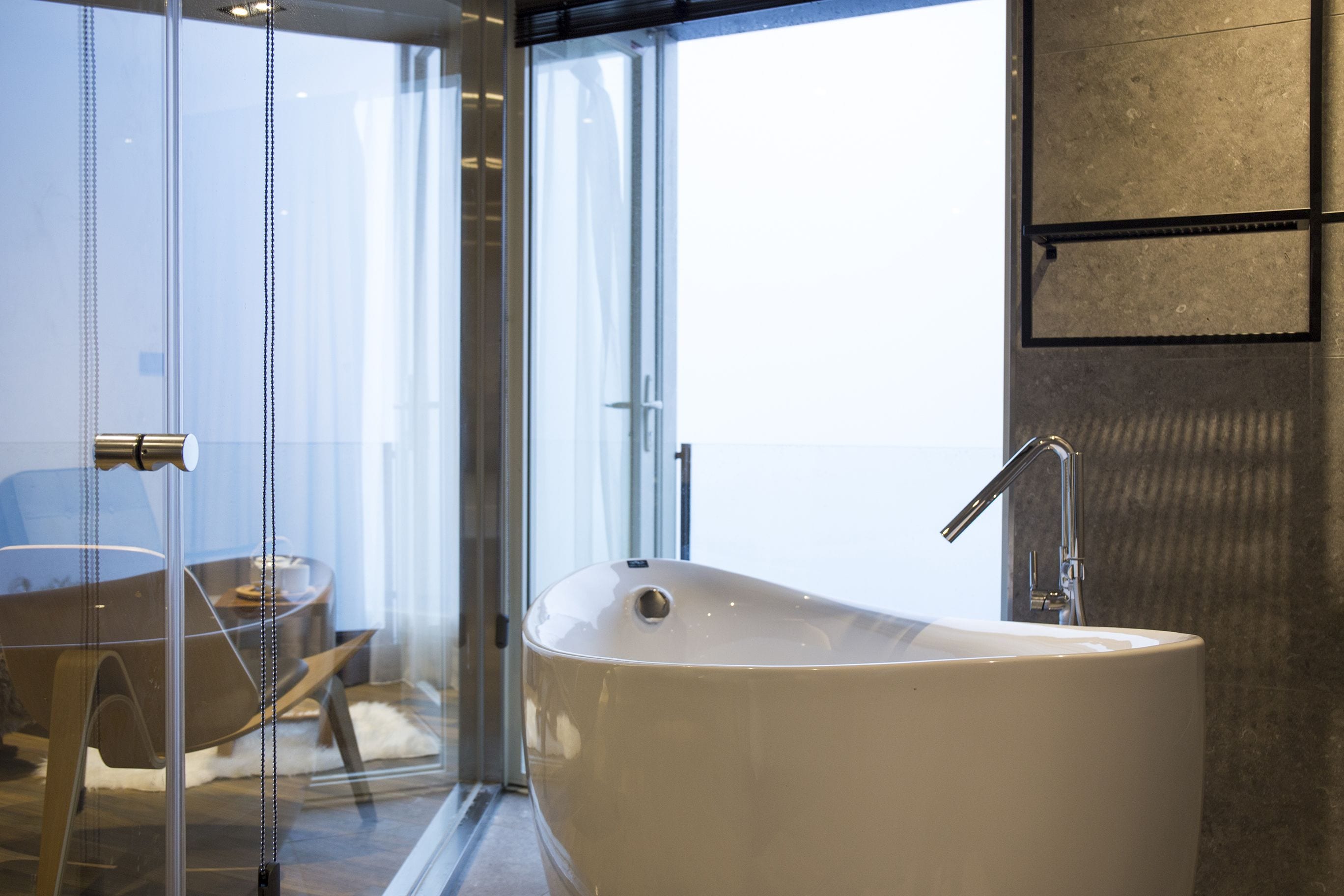 A modern bathroom with a freestanding bathtub, a glass shower enclosure, and a view of the outdoors.