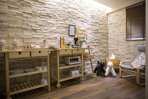 A room with a stone wall, a wooden table with kitchen items, a chair, and a small table with candles.