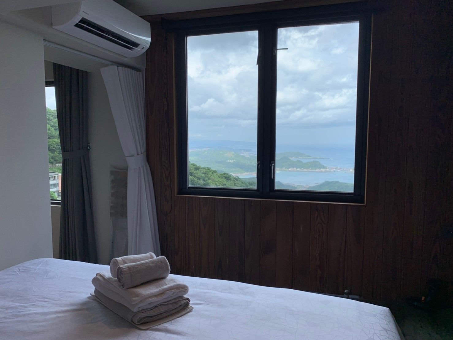 A hotel room with a large window offering a view of a coastal landscape.