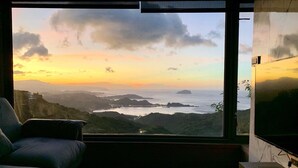 Un salon moderne doté d’une grande fenêtre donnant sur un paysage côtier au coucher du soleil.