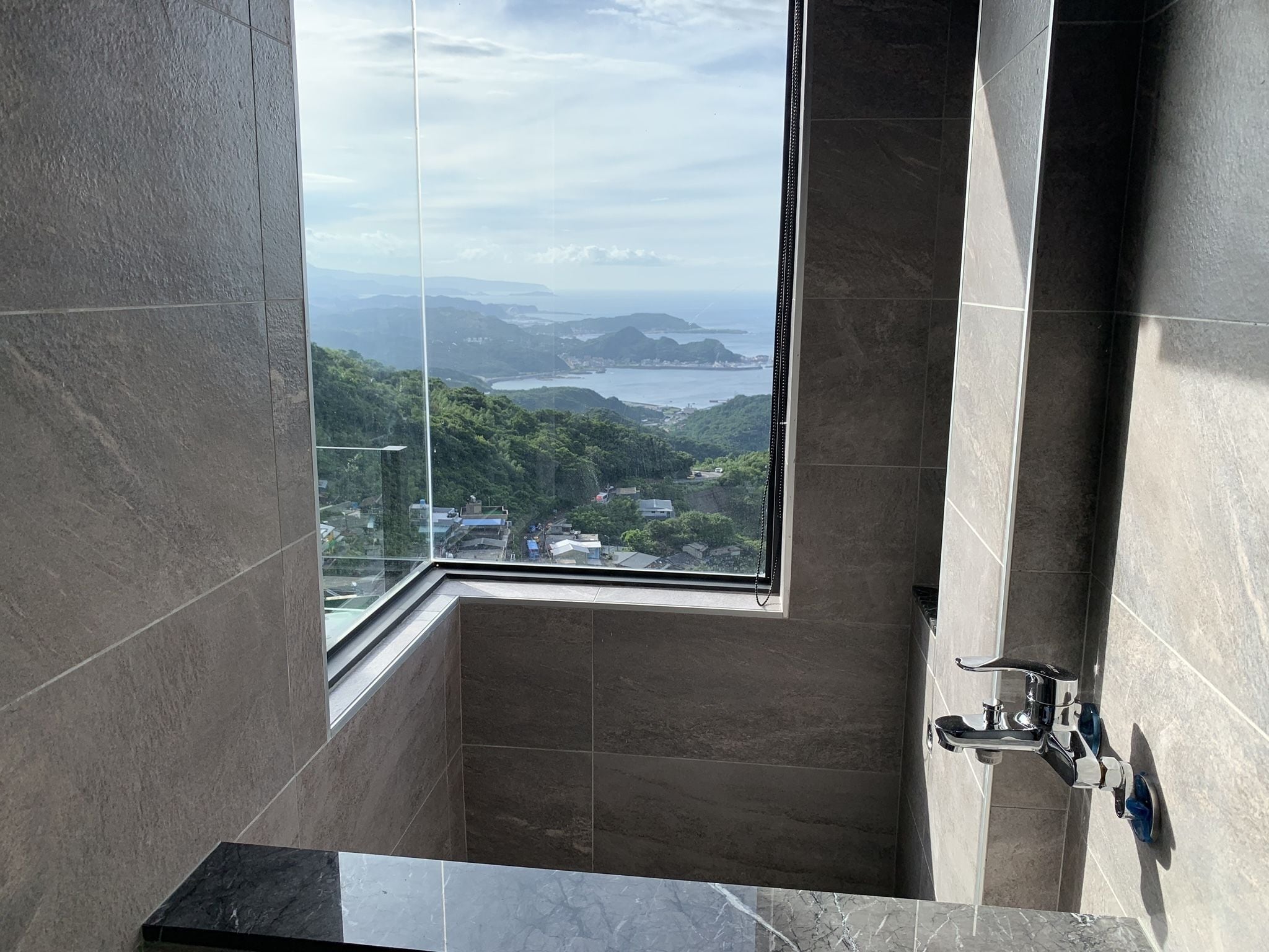 A bathroom with a large window offering a view of a coastal landscape.