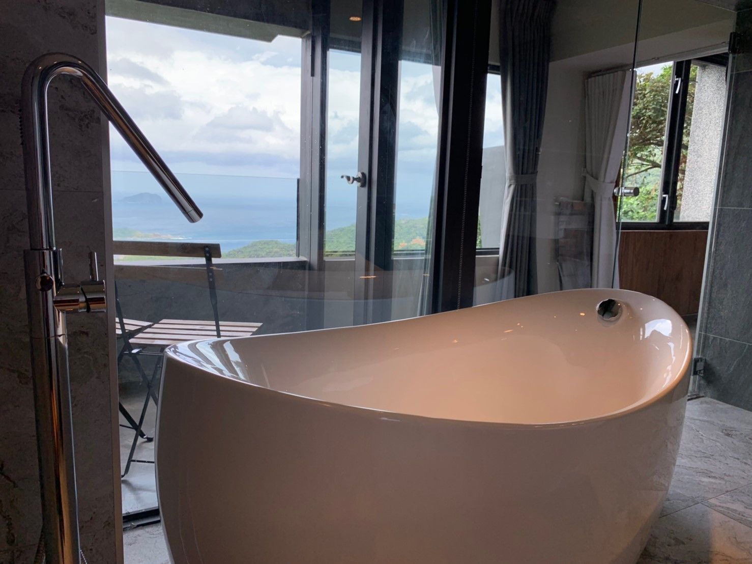 Un baño moderno con una bañera independiente, ventanas amplias que ofrecen vista al mar y un box de ducha de vidrio.