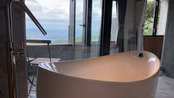 Un baño moderno con una bañera independiente, ventanas amplias que ofrecen vista al mar y un box de ducha de vidrio.
