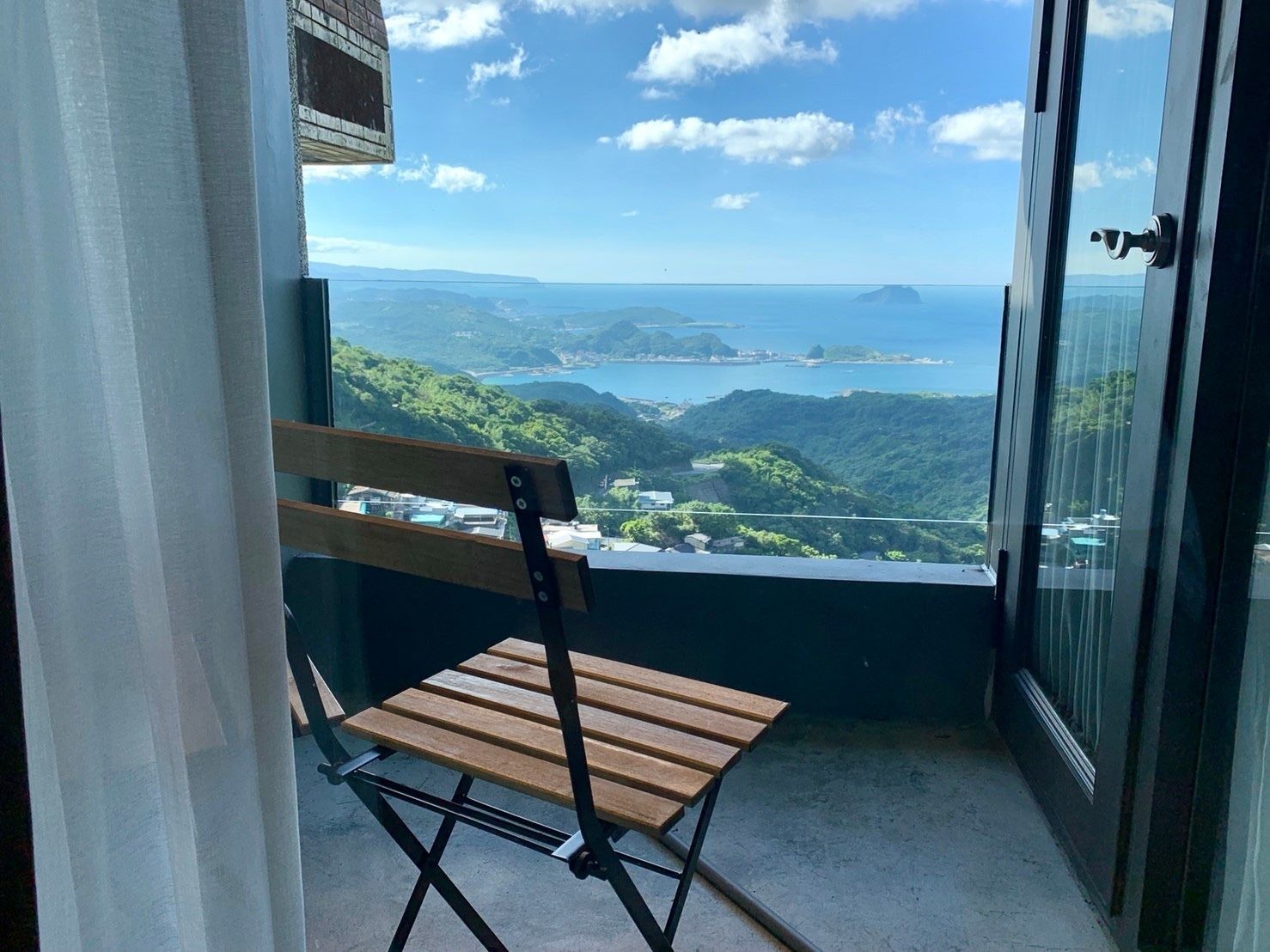 A balcony with a wooden chair and a view of a coastal landscape.