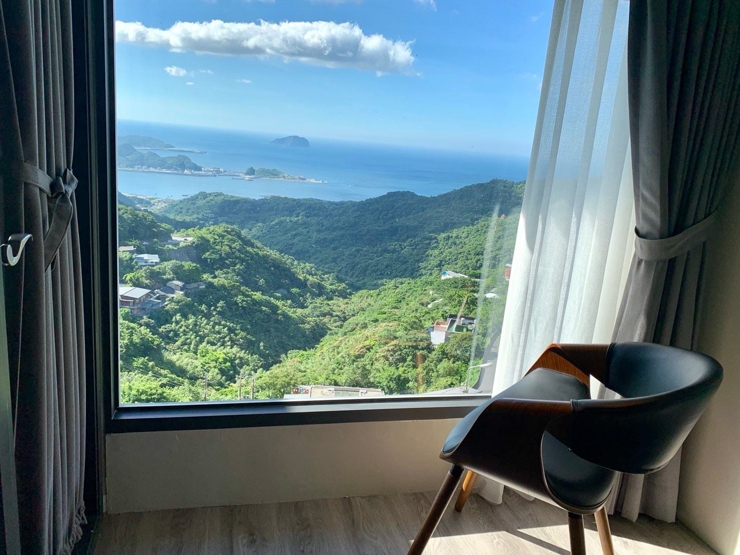 Ein Zimmer mit großem Fenster und Blick auf eine gebirgige Landschaft sowie das Meer.