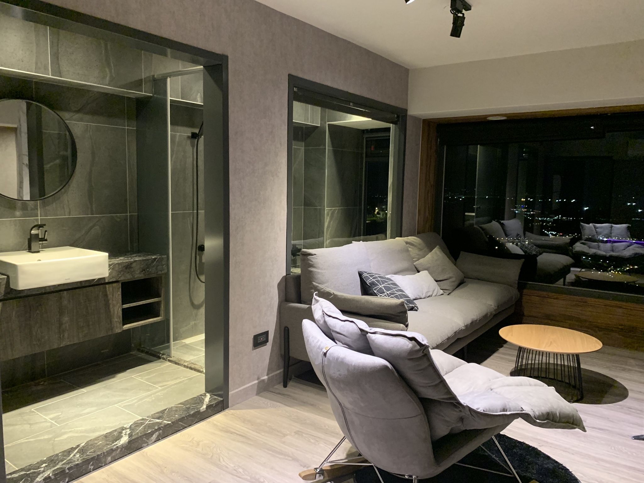 A modern living room with a grey sofa, a round coffee table, and a view of the city at night.