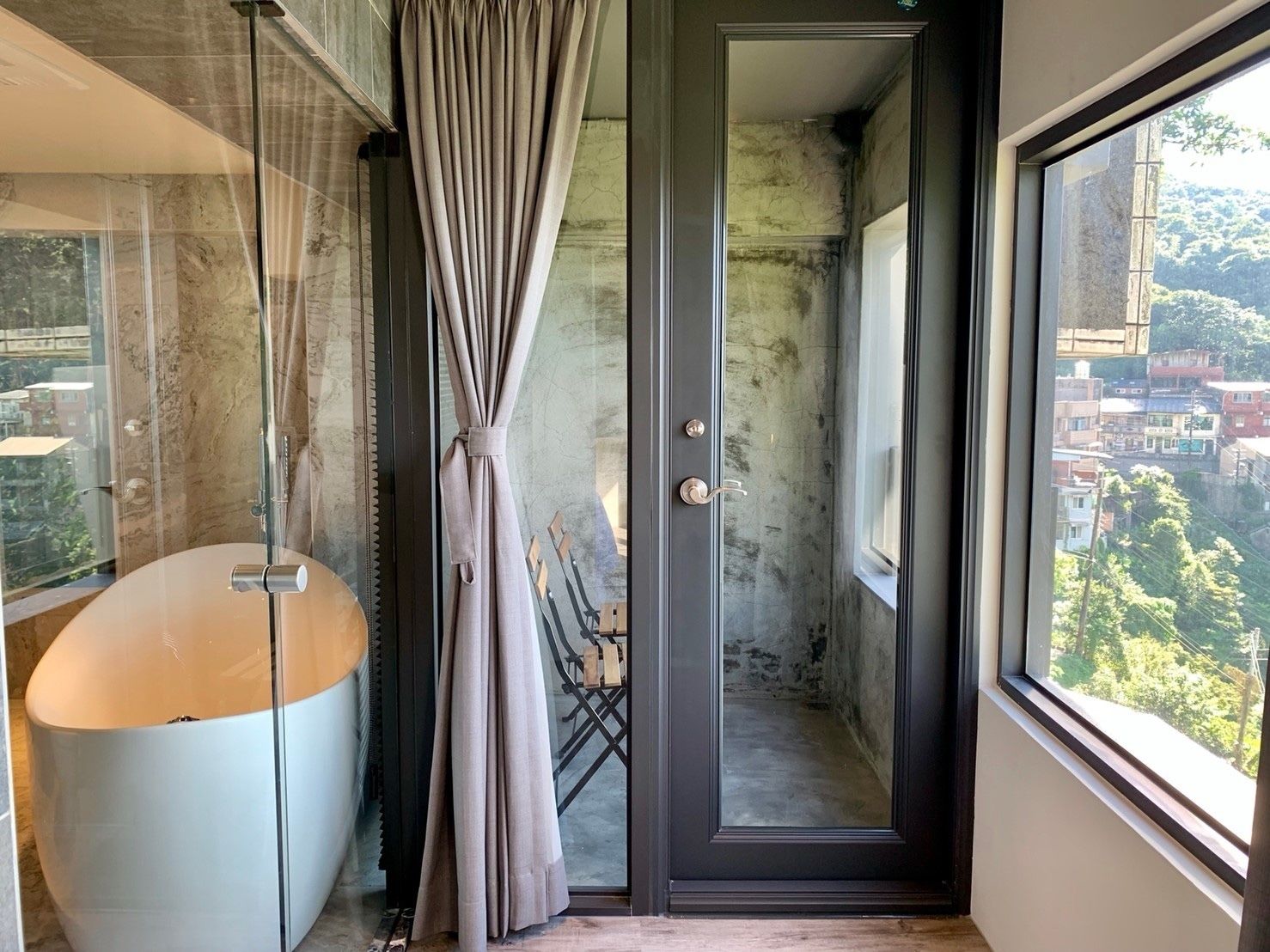 A modern bathroom with a freestanding bathtub, a glass shower enclosure, and a view of a cityscape through a large window.