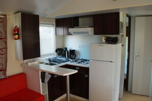 Una kitchenette compacta con estufa, pileta y microondas. Hay una silla roja y un extintor colgado en la pared.