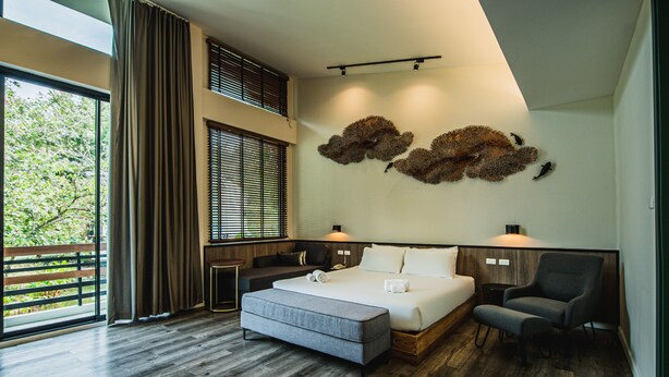 A modern hotel room with a large bed, a seating area, and a balcony with a view of trees. - Lumphawa Amphawa (Samut Songkhram)