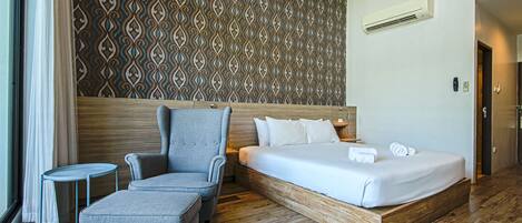 Una habitación de hotel con una cama, un sillón gris, una mesita y un papel tapiz estampado.