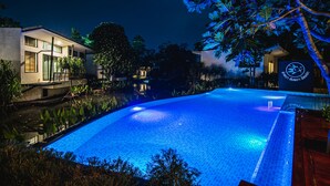 A nighttime swimming pool with a clear blue water surface, surrounded by lush greenery and modern buildings. - Lumphawa Amphawa (Samut Songkhram)