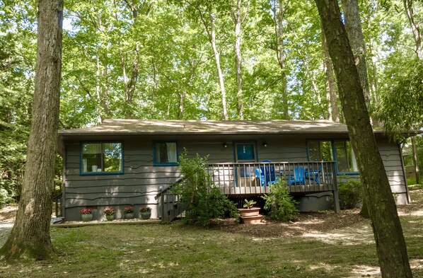 A single-story cabin with a front porch, surrounded by trees.
