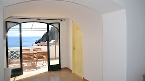 Habitación con vista al mar a través de un ventanal de vidrio, una puerta amarilla y piso de baldosas.