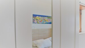 Un dormitorio con cama, paredes blancas y un cuadro colorido en la pared.