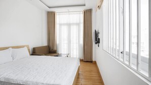 A hotel room with a large bed, a chair, a small table, and a TV mounted on the wall. - Adamas Apartment (Ho Chi Minh City)