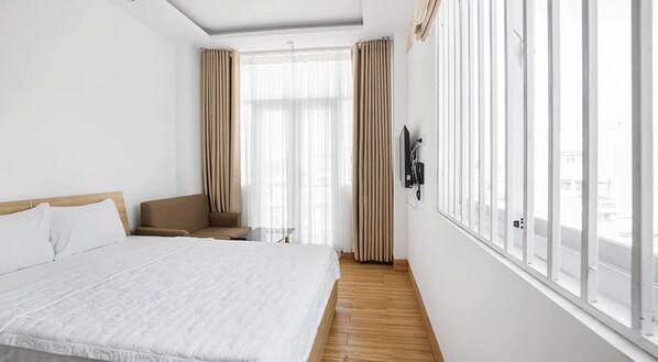 A hotel room with a large bed, a chair, a small table, and a TV mounted on the wall.