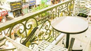 A balcony with a white table and metal railing, overlooking a busy street with various shops and buildings. - Adamas Apartment (Ho Chi Minh City)