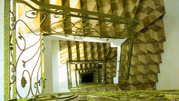 A spiral staircase with a geometric patterned wall and ornate metal railings. - Adamas Apartment (Ho Chi Minh City)