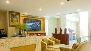 A hotel reception area with a marble reception desk, comfortable seating, a television displaying Netflix, and decorative items. - Adamas Apartment (Ho Chi Minh City)