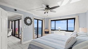 Une chambre dotée d’un grand lit, d’un ventilateur de plafond, d’une vue sur l’océan par les fenêtres et d’un balcon avec une chaise.