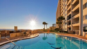 Une piscine avec un coucher de soleil en arrière-plan, entourée d’un bâtiment d’hôtel doté de balcons.