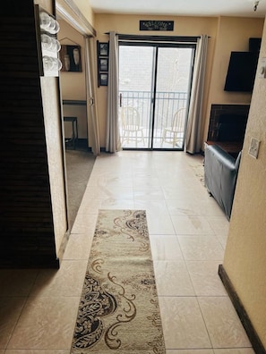 A hallway with a patterned rug, a sliding glass door leading to an outdoor area, and a television mounted on the wall. - 1 Br/ 1 Ba Mountain Central Condo (Park City)