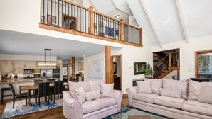 A spacious living area with a high ceiling and a balcony, featuring a kitchen, dining area, and seating with a glass coffee table. - Glen Lyon Lodge | Spacious 5BR Vail Home, Cascade Lift #20 (Vail)