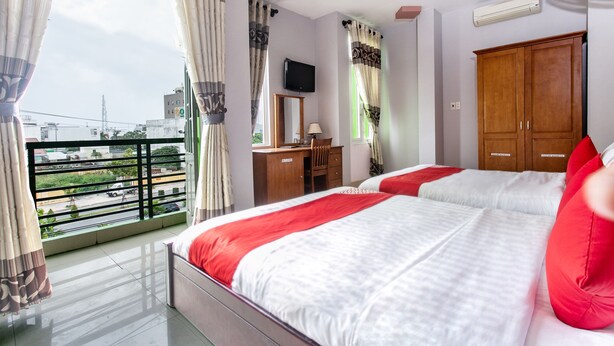 Quarto de hotel com varanda, cama com roupa de cama vermelha e branca, guarda-roupa de madeira e secretária com espelho.