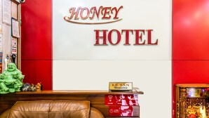 Uma mesa de recepção com uma placa que diz "HONEY HOTEL" e uma placa "LE TAN Reception" acima.