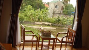 A balcony with wooden chairs and a table, overlooking a garden with banana trees and a small pond. - Ninh Binh Riverside Homestay 2 (Ninh Binh)